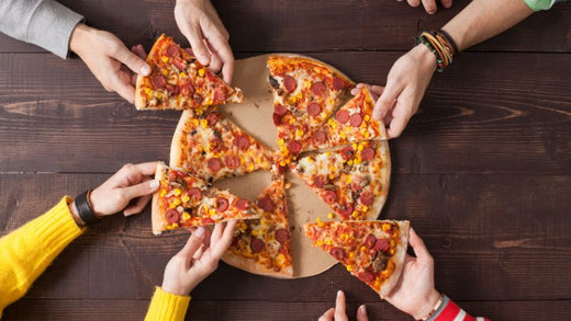 Six hands grabbing pepperoni pizza slices from a wooden table.