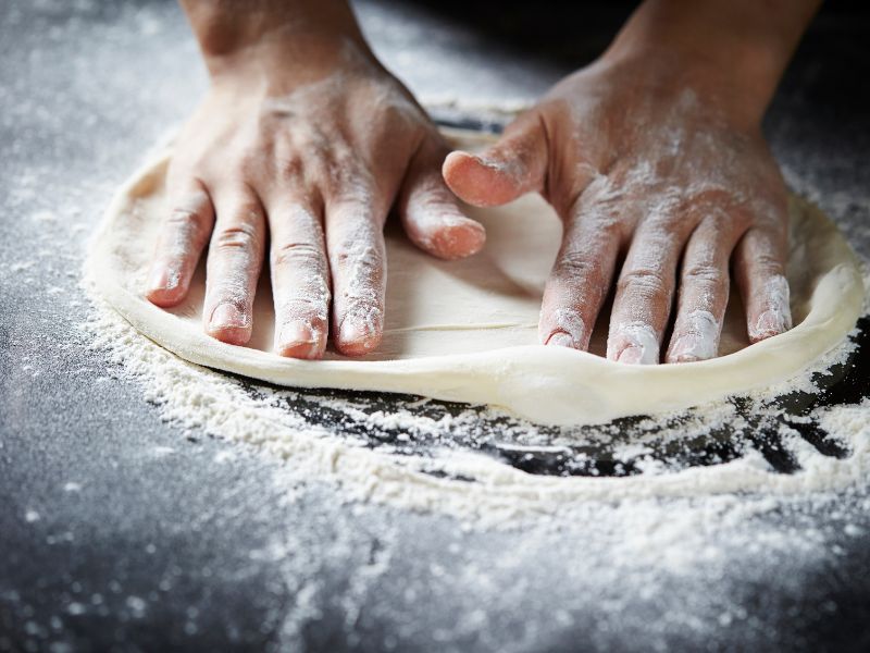 Two hands flatten dough on a floured surface.