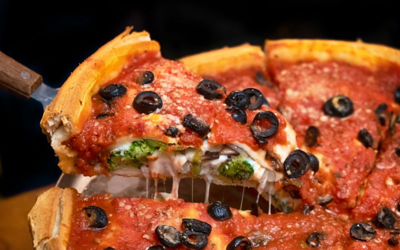 A mouthwatering, deep-dish pizza slice loaded with tomato sauce, melted cheese, and black olives on top of a golden-brown crispy crust.