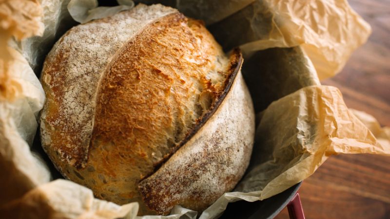 A crusty round loaf rests in a parchment-lined baking dish.