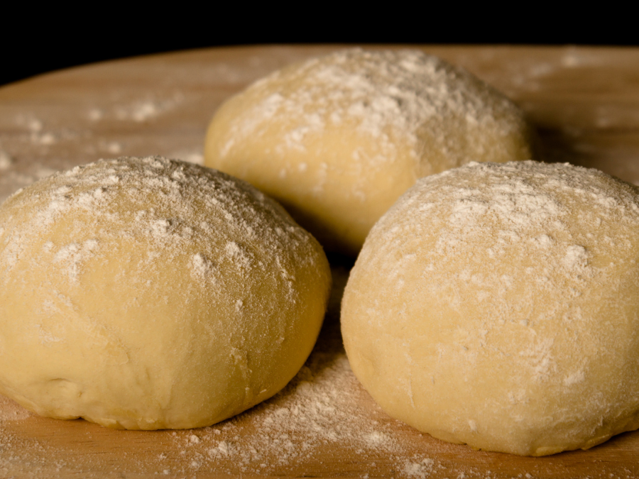 Three round balls of raw dough dusted with flour resting on a wooden surface.