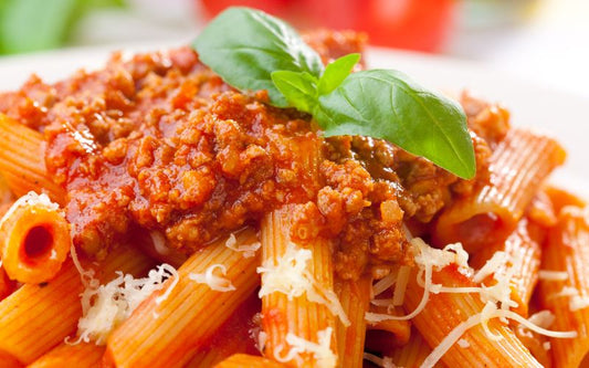 Penne pasta with meat sauce, grated cheese, and a basil garnish.