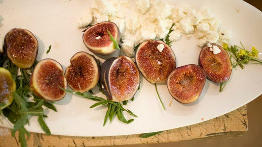 Sliced figs, crumbled cheese, and greens on a white plate.