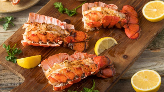 Three seasoned lobster tails on a board, garnished with parsley and lemon wedges.