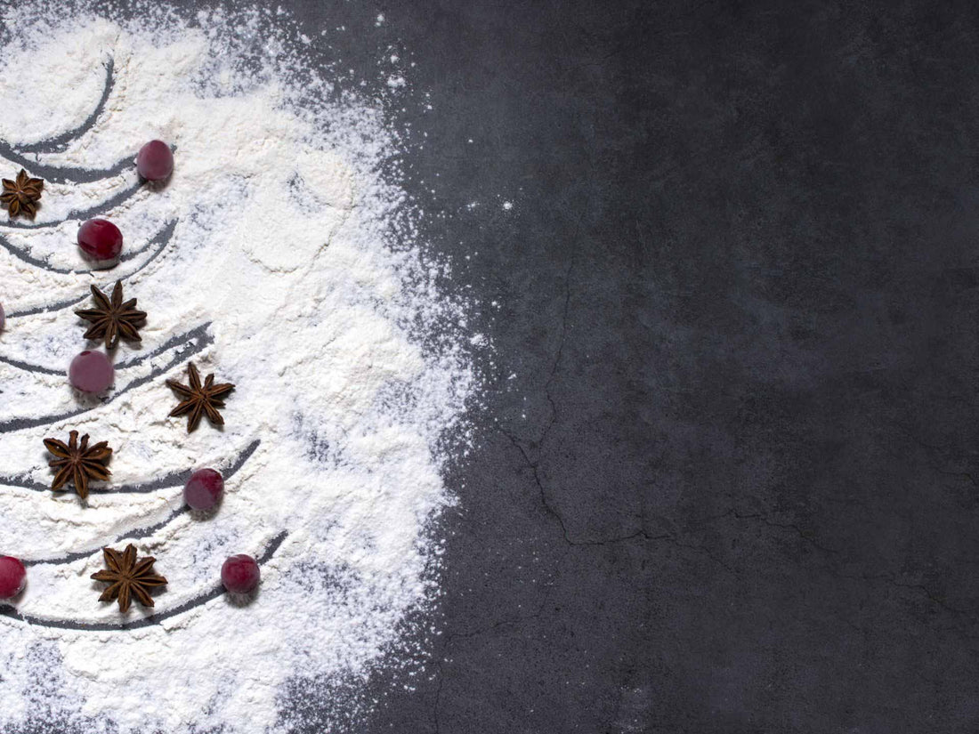 A Christmas tree shape in powdered flour on a dark surface, adorned with star anise and red berries.