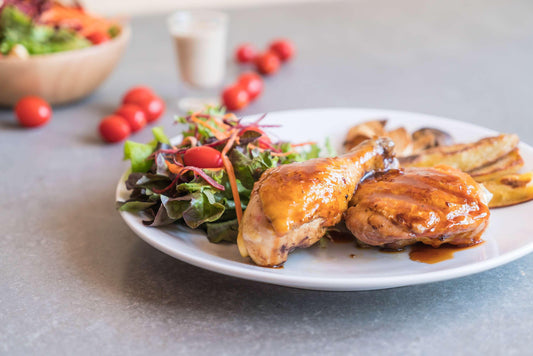 A meal of roasted chicken, fresh salad with cherry tomatoes and mushrooms, with extra salad and cherry tomatoes in the background.