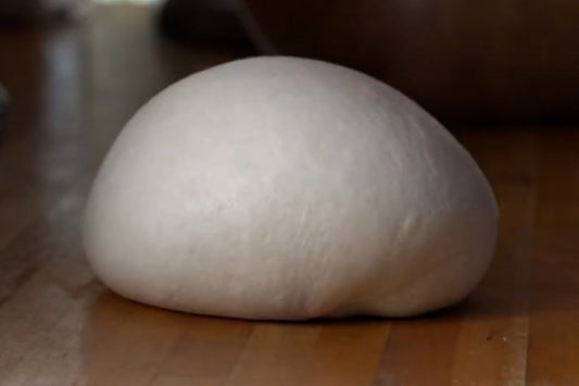 A smooth, white dough ball rests on a wooden surface.