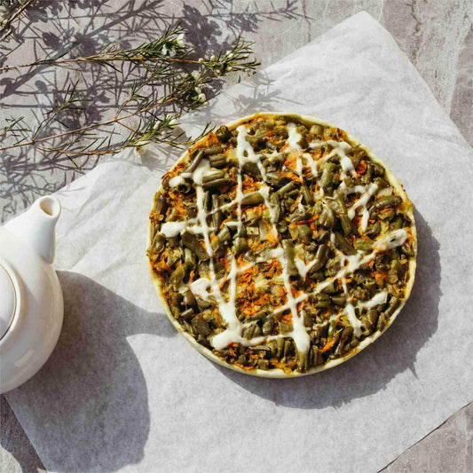 A vegetable tart with sauce on parchment, beside a white teapot.