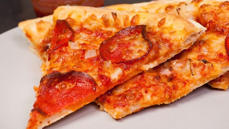Pepperoni pizza slices with melted cheese and onions on a plate.