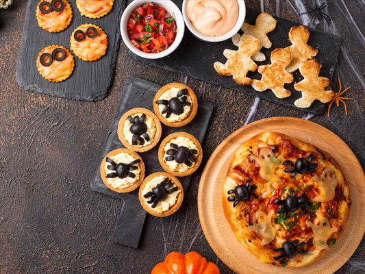 Halloween-themed snacks cover the table: spider crackers, mummy pizzas, ghost mini pizzas, and dip with mummy-shaped crackers.