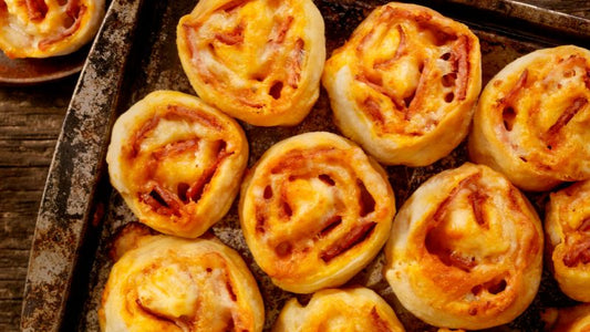 Freshly baked pizza pinwheels on a tray with golden pastry, melted cheese, and pepperoni layers.