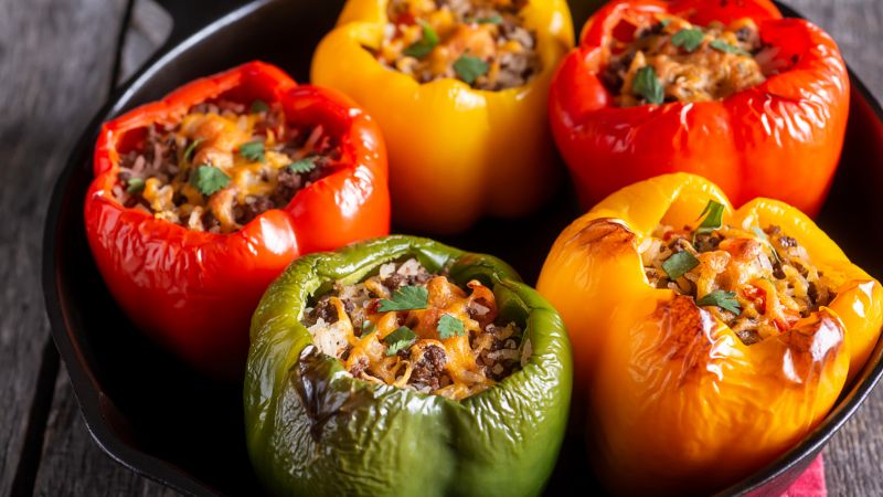 A skillet with five colorful stuffed bell peppers topped with melted cheese and cilantro.
