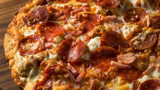 A close-up of a thin crust pizza with pepperoni, sausage, ham bits, and melted cheese.