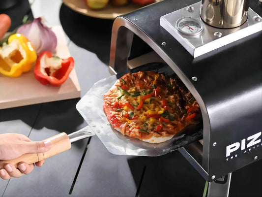 Someone uses a pizza peel to remove a freshly baked, topped pizza from the pizzello oven.