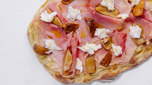 Flatbread with ham, cheese, and mushroom on a white surface.