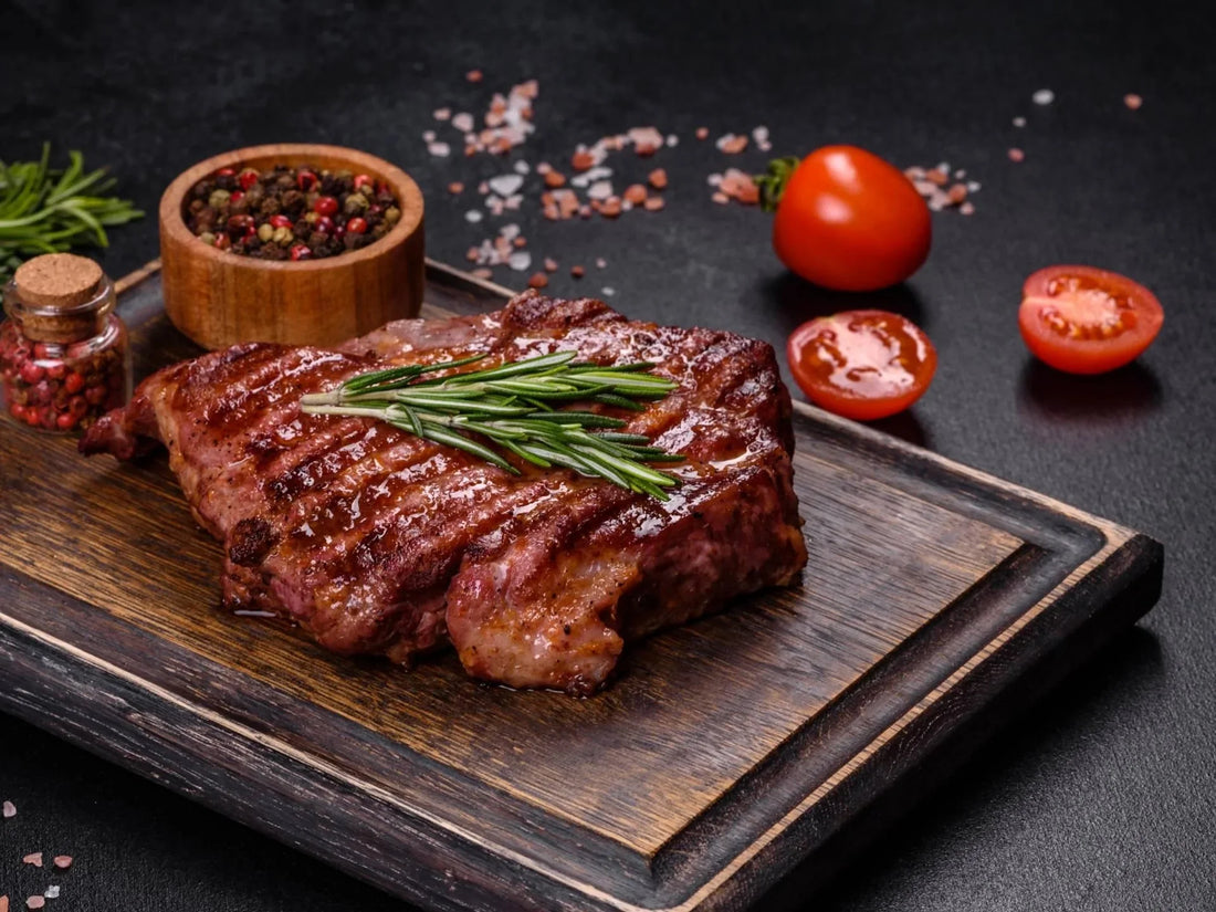 Ribeye Steaks with Grilled steak with rosemary, peppercorns, sea salt, and sliced tomatoes on a wooden board.Butter - Pizzello