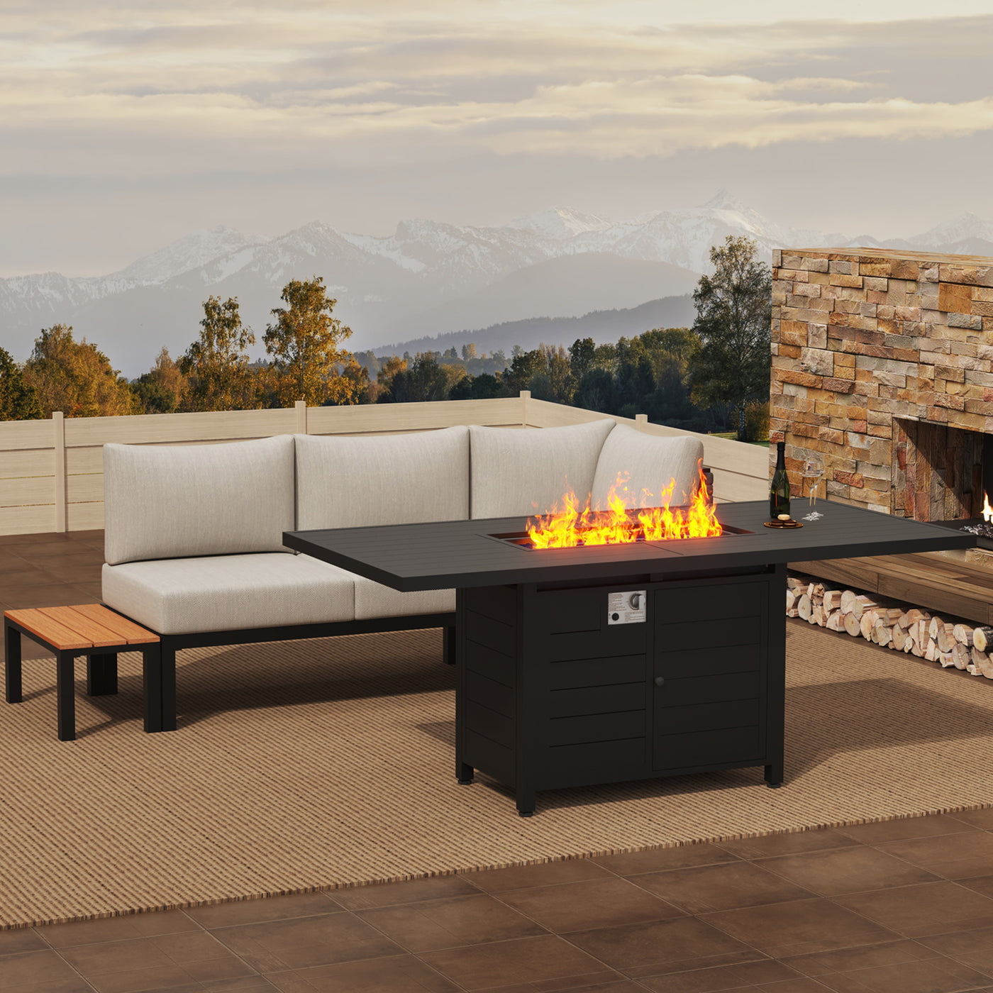 Patio with beige sectional, stone fireplace, and Pizzello Passione 62.5" fire pit table, set in trees and mountains.